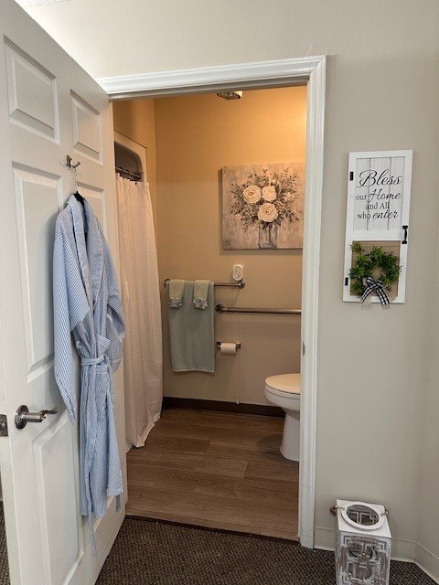A bathroom with a toilet, a shower curtain, a towel, and a robe hanging on the door at Spring Arbor of Rocky Mount